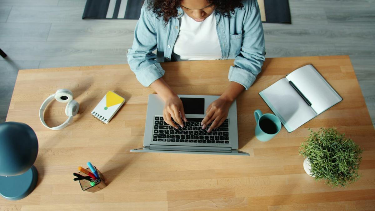 Overhead view of a writer typing on a laptop at a wooden desk with a notebook, coffee and headphones