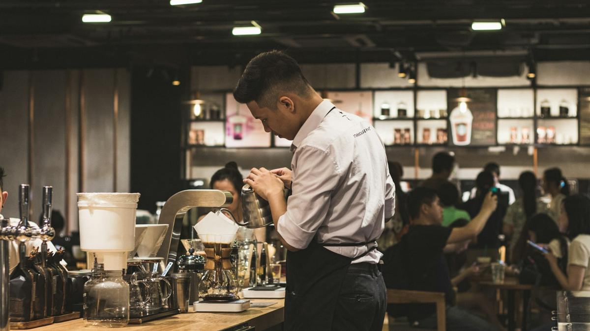 A cafe worker preparing drinks behind a busy coffee counter