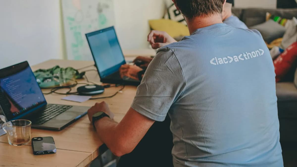 Two developers working side by side on laptops at a wooden table during a coding session