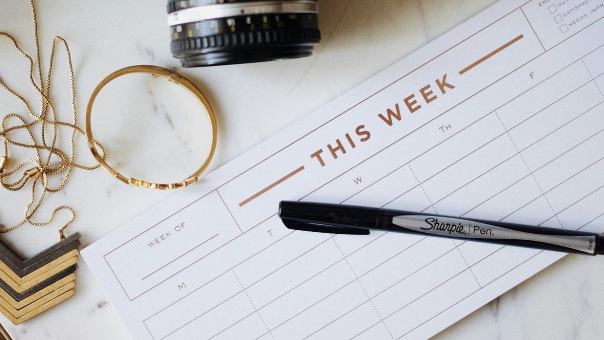 A weekly paper planner with a pen, camera and desk accessories