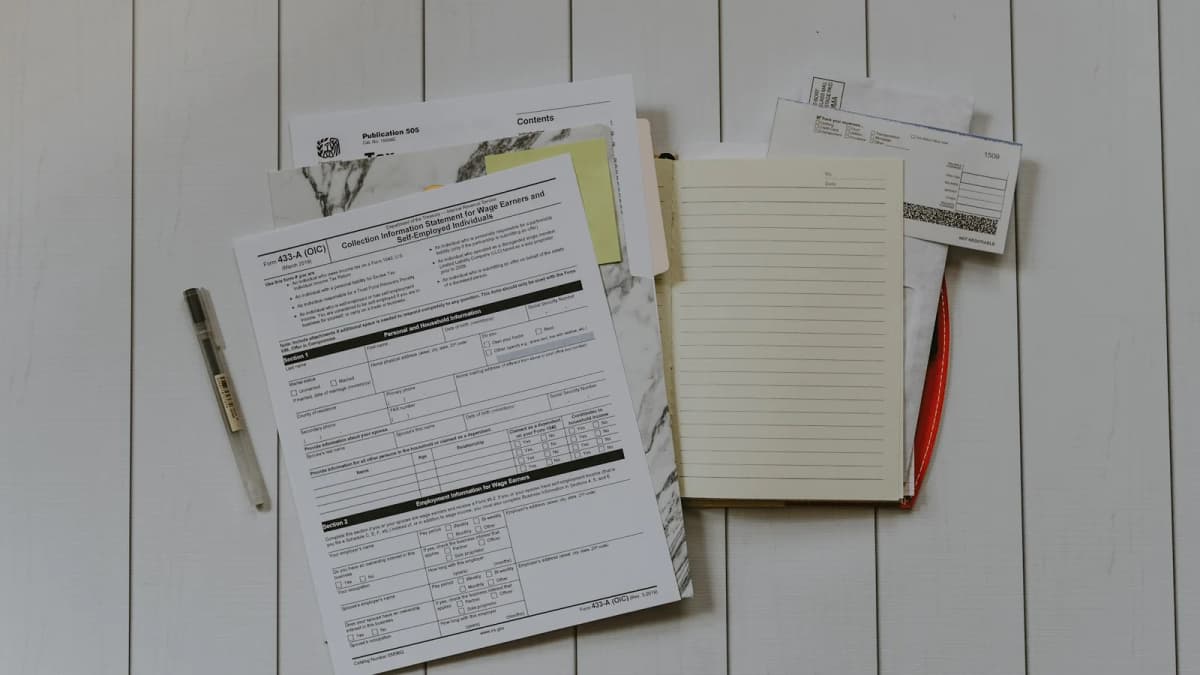 Unfilled financial forms, a notebook and a pen arranged on a white wooden table