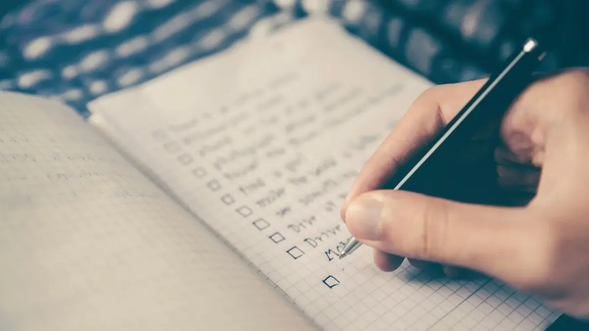 A person writing a checklist in a squared-paper notebook with a black pen