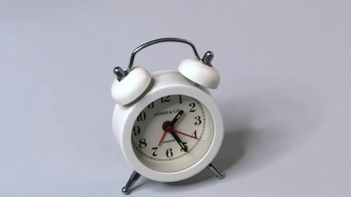 A small white twin-bell alarm clock standing on a plain grey surface