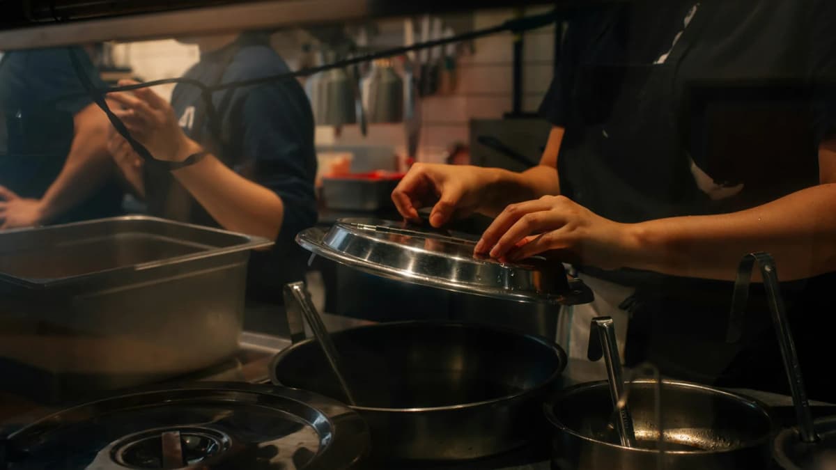 Restaurant staff work together around a steaming pot in a professional kitchen