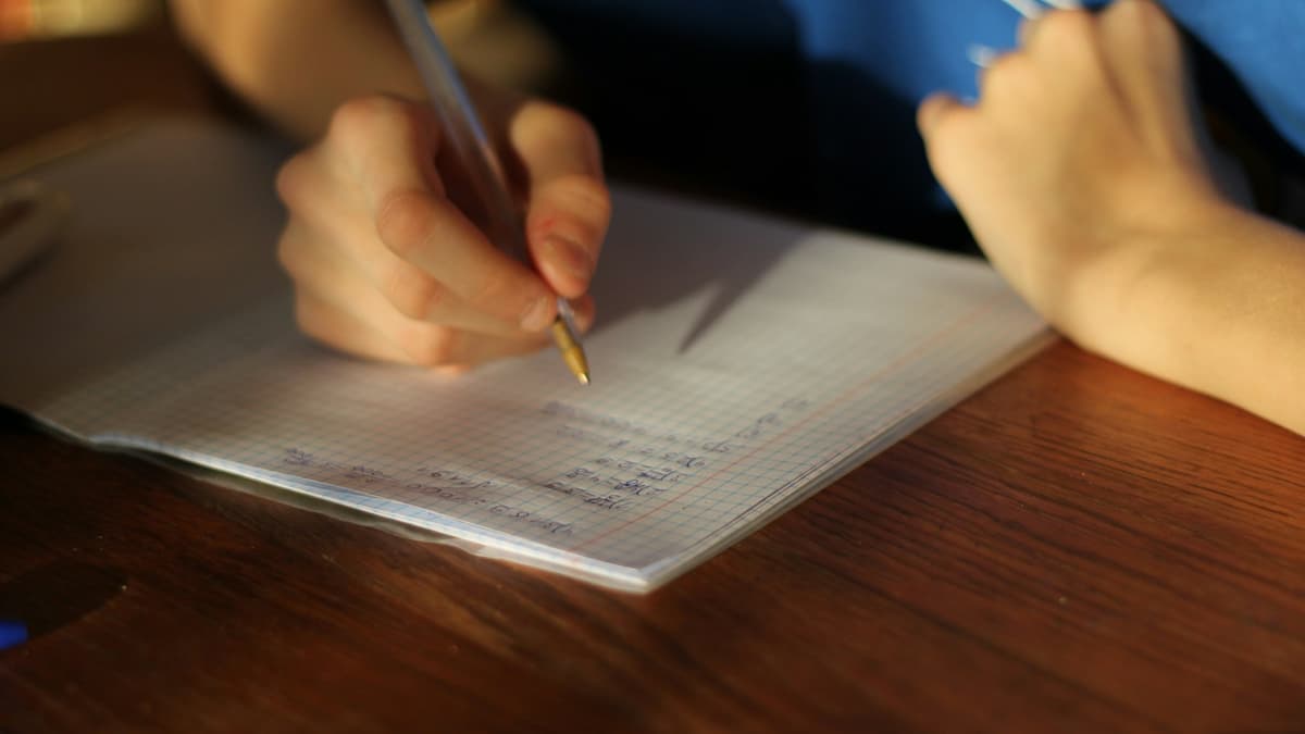 A person using a pen to write notes in a squared notebook on a wooden table