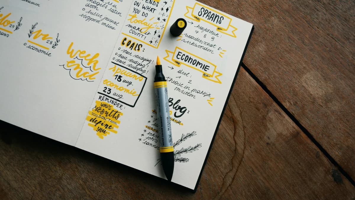 A handwritten weekly journal with colored headings and pens on a desk