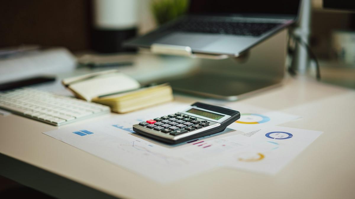 A calculator and financial charts beside a laptop and notebooks on a desk